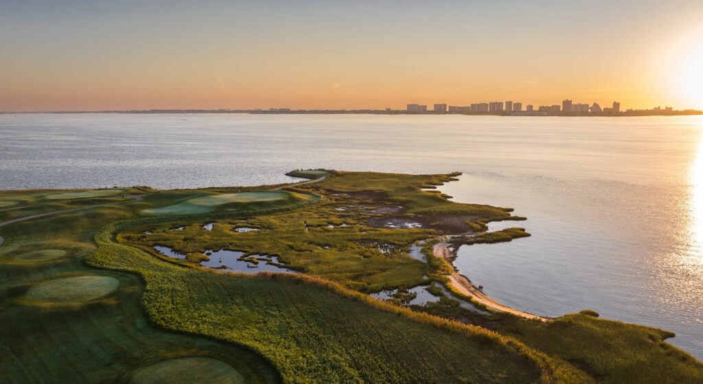 the sun is setting over a golf course near the water