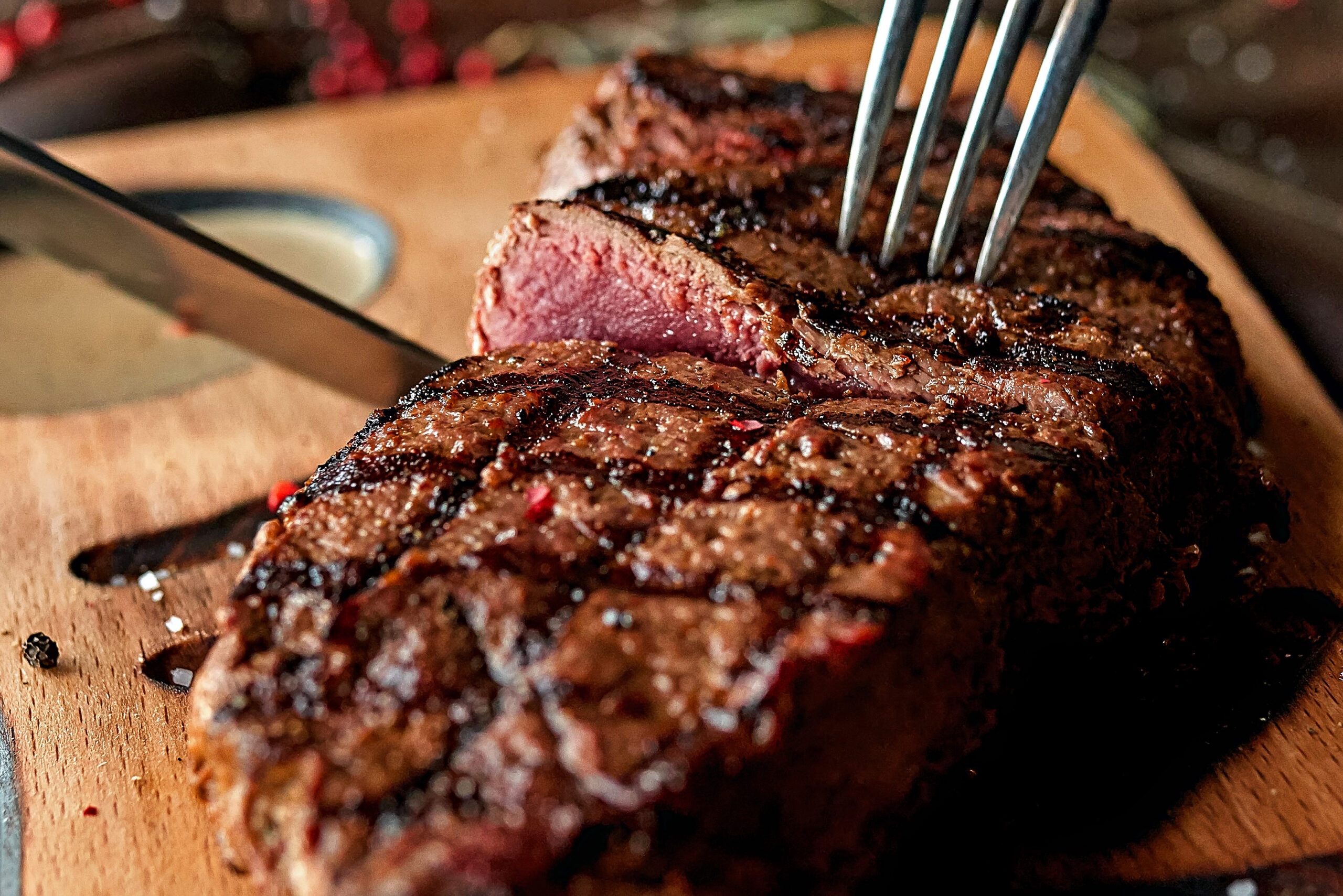 A plated tenderloin steak cut open to reveal a medium-rare center, served with roasted vegetables alongside a glass of red wine on a white tablecloth.
