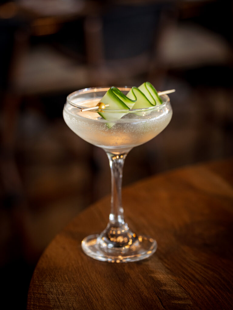 a cocktail with cucumber garnish on a wooden table