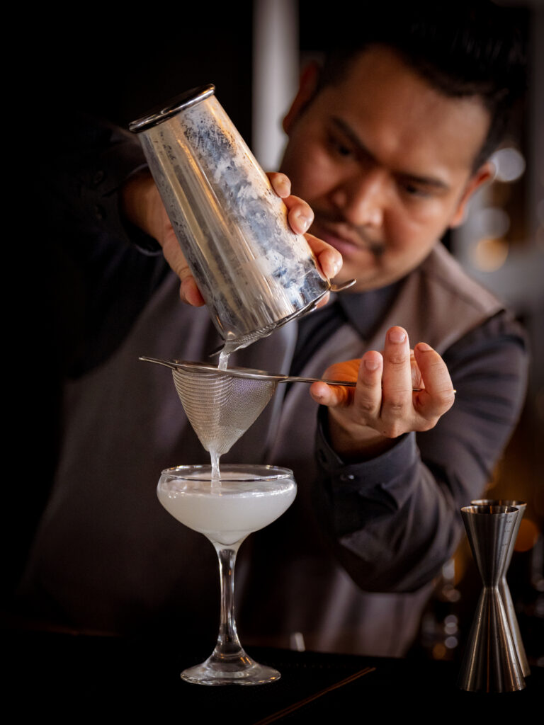 a man pouring a drink into a martini glass